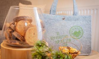 A gray felt bag stands next to a glass with baked pastries. In the bag, the text reads "We are on the trail of the Kraut Prince."