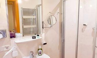 A modern bathroom with a shower and a sink. The walls are tiled in light colors and there is a large mirror.