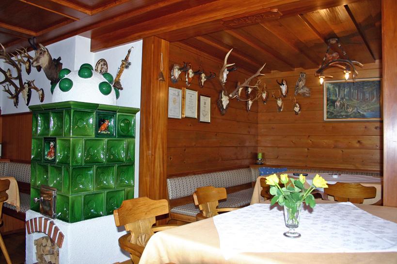 A cozy dining room with wooden furniture and a green tiled stove. Hunting trophies and pictures hang on the walls.