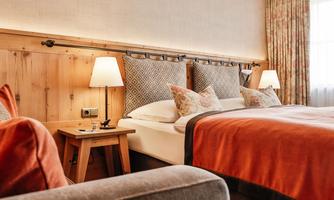 A cozy room with a double bed, upholstered with colorful cushions. Warm colors and soft light create an inviting atmosphere.