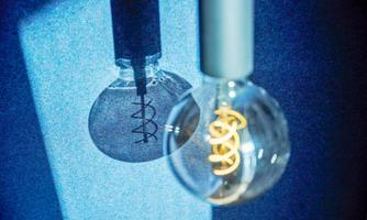 A glowing light bulb hangs, with a circle of light inside it. Its shadow is fascinating to see on the wall.