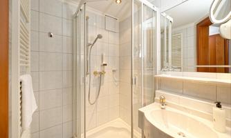A modern bathroom with a glass shower and bright tiles. The wash area is clean and well-lit.
