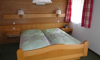 A simple bedroom with two beds and wooden decor. This includes red accent pillows and a window with curtains.