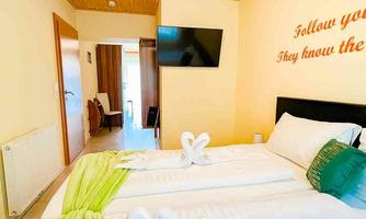 A bright room with two beds and a wooden ceiling. The bedding is white with green accents, and a television is mounted on the wall.