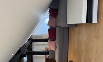 A cozy living room with a gray sofa and red cushions. The room has wooden flooring and a sloping ceiling.