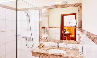 A modern bathroom with a glass shower enclosure and an elegant sink. In the background, a wooden space is visible, exuding coziness.