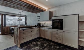 A modern kitchen with wooden elements and stylish appliances. Large windows offer a view of the mountains.