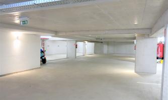 An empty parking space in an underground garage with bright lighting and concrete walls. There are some fire extinguishers mounted on the walls.