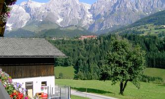 A picturesque landscape with majestic mountains in the background. In the foreground, there is a house with colorful flowers and a meadow.