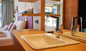 A modern room with a minimalist ceramic sink. In the background, light wood and cozy beds can be seen.