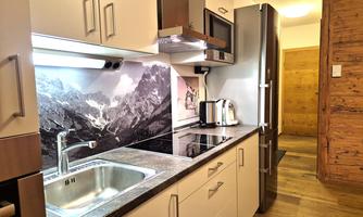 A modern kitchen with elegant cabinets and a granite countertop. In the background, a mountain landscape is visible as wall design.