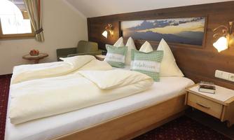 A cozy bedroom with a large double bed and comfortable pillows. The warm wood design and soft lighting create an inviting atmosphere.