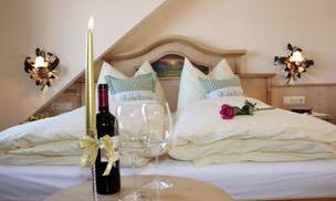 A cozy room with two beds, white bedcovers, and decorative pillows. On the table are a red wine, two glasses, and a rose.