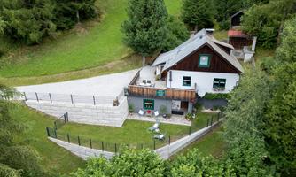 A cozy house surrounded by green trees and meadow. The outdoor area is equipped with a fence and seating.