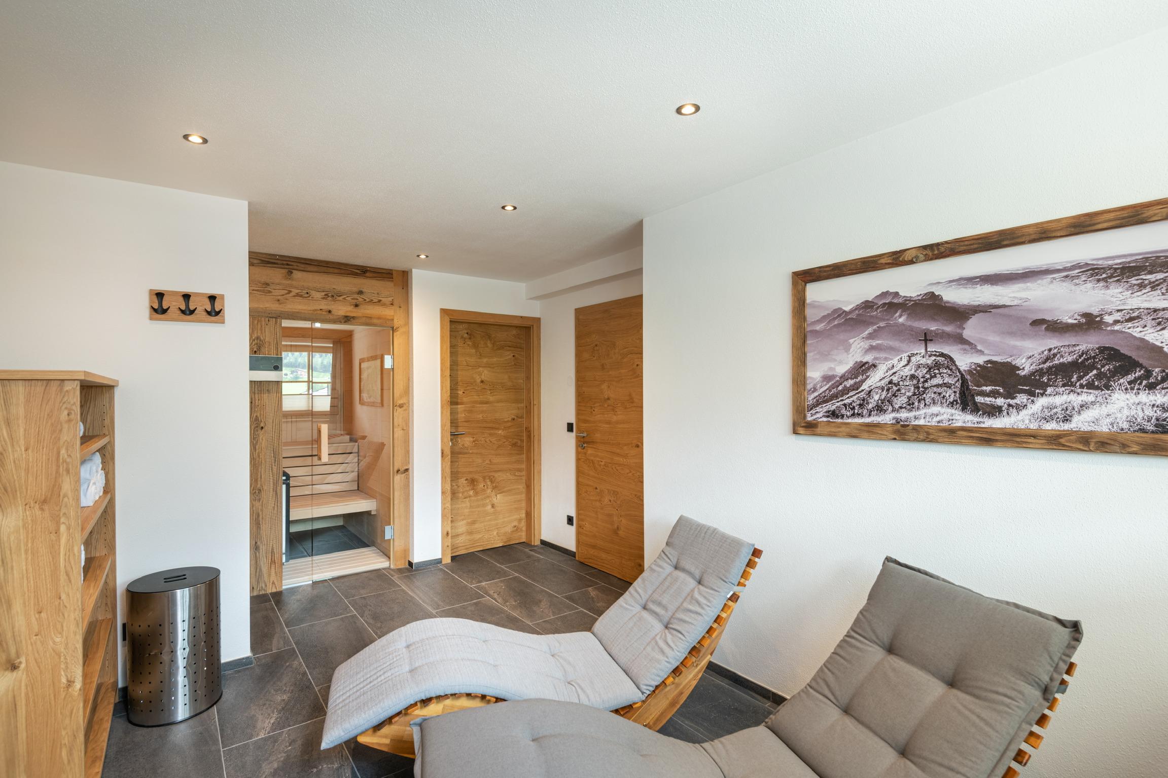 A cozy room with modern loungers and wooden details. The room is bright and inviting, with a view of beautiful wall art.
