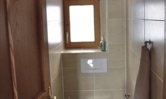 A small bathroom with a toilet and a sink. There is a window and a brown door.
