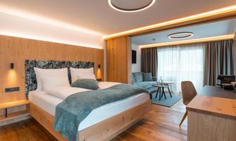 A modern hotel room with a large double bed and elegant wood paneling. The room is bright and welcoming with a cozy seating area.