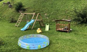 An outdoor playground with a slide, a swing set, and a wading pool. The lawn is green and well-maintained.