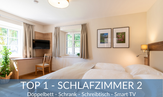 A bright bedroom with a double bed, wardrobe, and desk. There is also a smart TV and a window with a view.