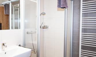 A modern bathroom with a shower cabin and a sink. Towels hang on the wall, and a towel warmer is available.