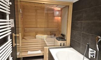 A modern bathroom with a wooden sauna and a bathtub. The walls are tiled in dark colors, creating a relaxed atmosphere.