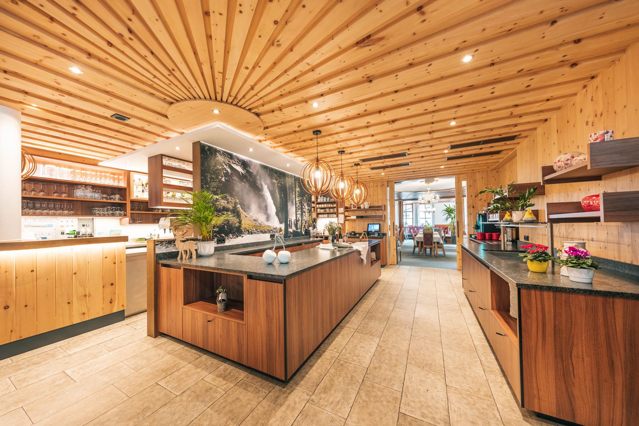 A modern restaurant with wooden paneling and stylish light installations. The space is bright and inviting, featuring a large window that looks outside.