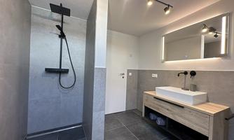A modern bathroom with an open shower. There is a stylish sink and bright lighting.