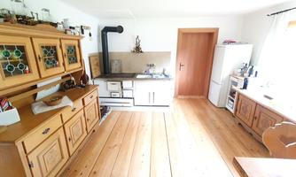 A cozy kitchen with wooden cabinets and a traditional stove. The floor is made of light wood and the light falls gently through the window.