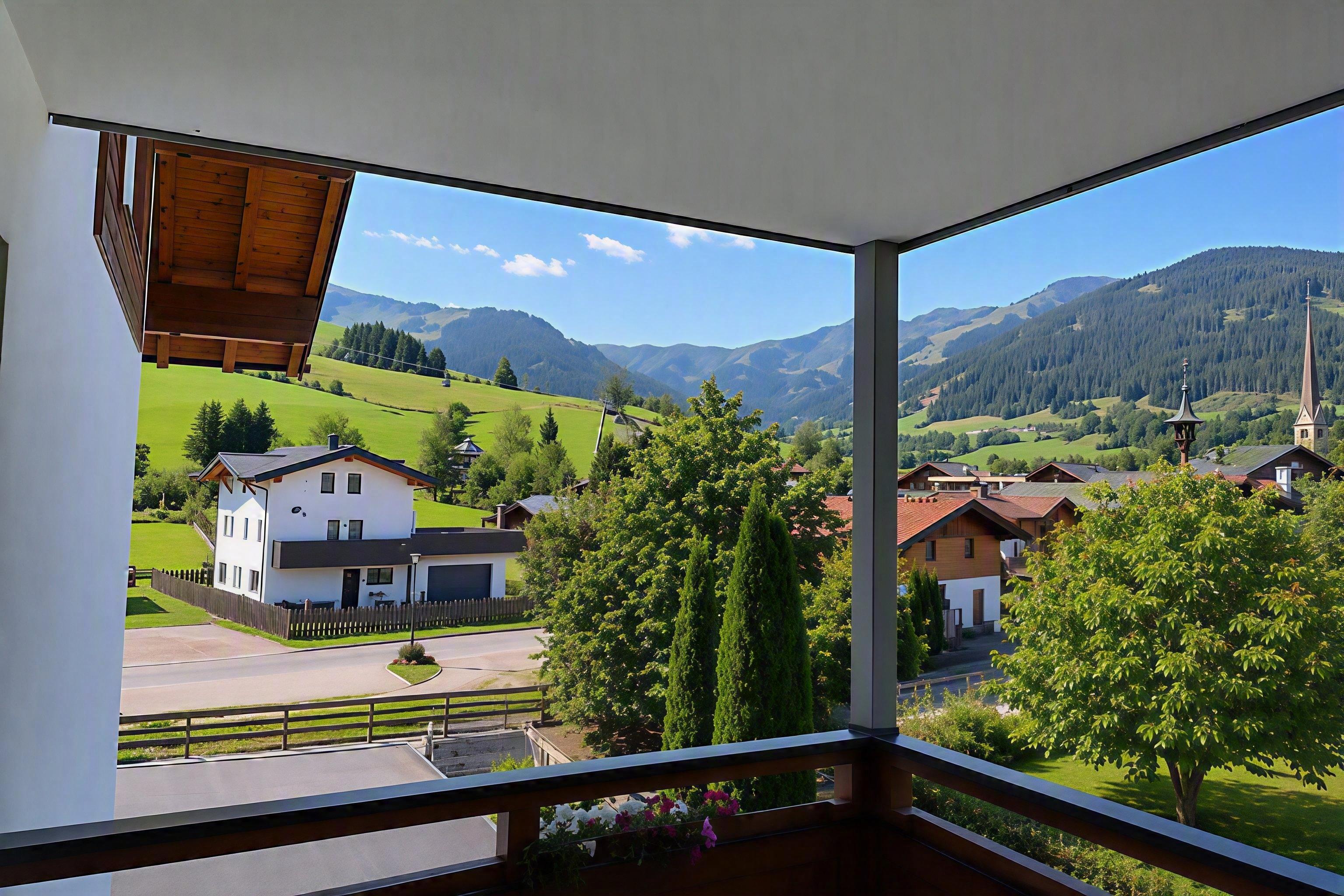A view from a balcony of green hills and traditional houses. In the background, mountains and a blue sky are visible.
