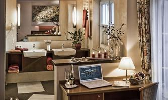 A modern bathroom with two sinks, stylish lamps, and plants. A cozy workspace with a laptop and glasses harmoniously integrates into the room.