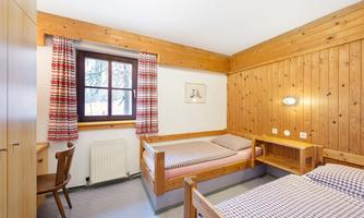 A cozy bedroom with two single beds and wooden paneling.  
Large windows let in plenty of light and create an inviting atmosphere.