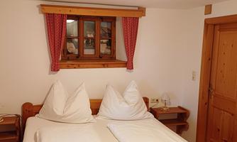 A cozy bedroom with two beds and traditional pillows. The room has wooden paneling and a window with red curtains.