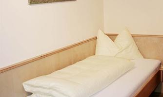 A simple bedroom with a single bed and two large pillows. On the wall hangs a picture of horses in a landscape.