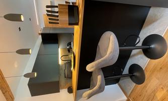 A modern kitchen with a bar counter and two comfortable stools. The decor is in black and natural wood tones.