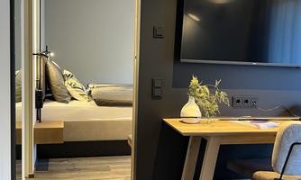 A modernly furnished room with a comfortable bed and a desk. There is a large television and a pleasant atmosphere.