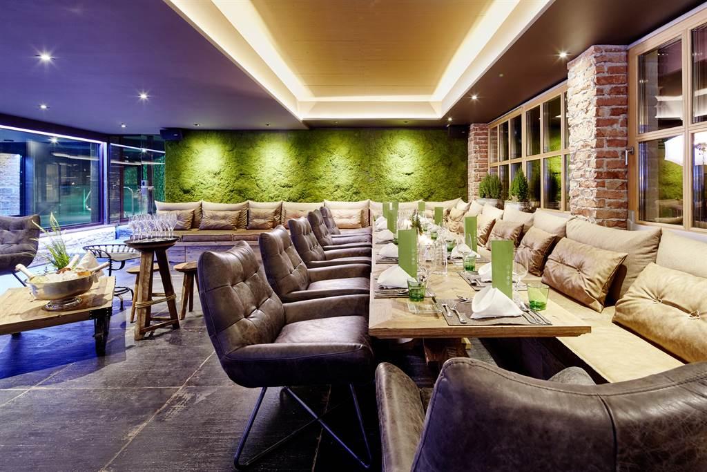 A stylish restaurant with cozy leather armchairs and a long table. The walls are decorated with plants, creating a relaxed atmosphere.