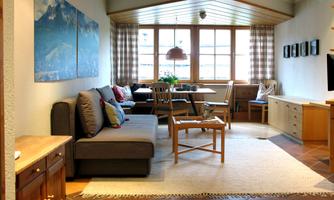 A cozy living room with a couch, a table, and large windows. The warm colors and the decoration create an inviting atmosphere.