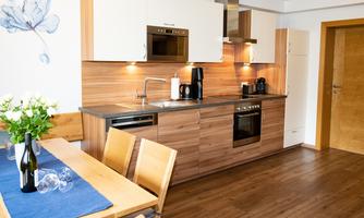 A modern kitchen with wooden surfaces and stainless steel appliances. The dining area is furnished with a table and chairs, and there are fresh flowers on the table.