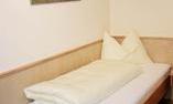 A simple room with a single bed and a white bedspread. On the wall hangs a picture of a horse in a rural landscape.