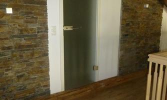 A modern hallway with a wooden floor and a glass door. The walls are clad in natural stone, giving the room a cozy atmosphere.