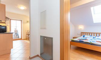A bright hallway with access to a bedroom and a kitchen. The floor is made of wood and there is a large window that lets in light.