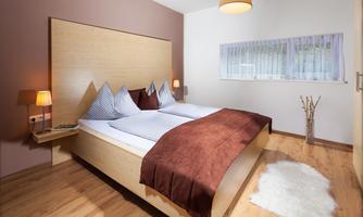A cozy bedroom with a double bed and wooden floor. The walls are painted in soft colors, and there is gentle lighting.