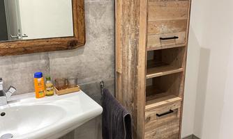 A modern bathroom with a vanity and a tall wooden shelf. The mirror has a rustic frame and the floor is tile-like.