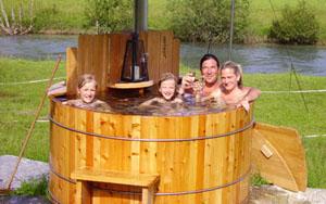 A family is relaxing in a wooden tub outdoors. They are smiling and enjoying their time in nature.