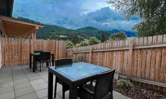 A cozy terrace with tables and chairs. In the background, green hills and a cloudy sky are visible.