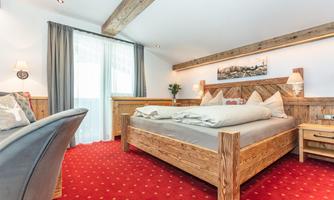 A cozy bedroom with a wooden bed and red carpet. The bright curtains provide plenty of daylight and a welcoming atmosphere.