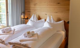 A cozy bedroom with two beds, white blankets and pillows.  
On the wall, there are wooden panels and there are windows with curtains.