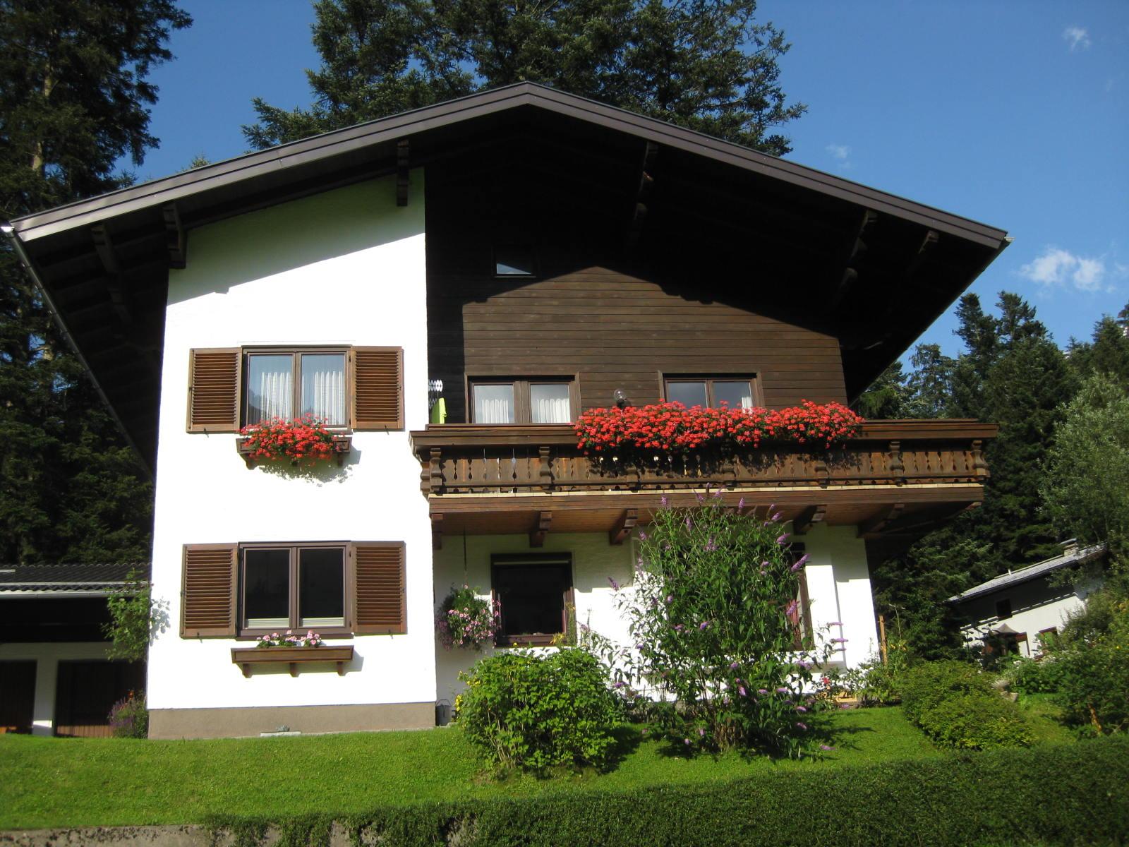 A beautiful multi-story house in a green environment. It has a balcony with flowers and modern architecture.