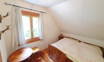 A cozy bedroom with a large bed and a small table. The window offers a view of nature.