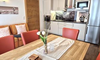 A modern kitchen with a dining area and cozy living space. The table is beautifully decorated with a vase and fresh flowers.